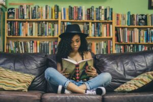 Woman wearing hat. She's sitting on a couch reading.